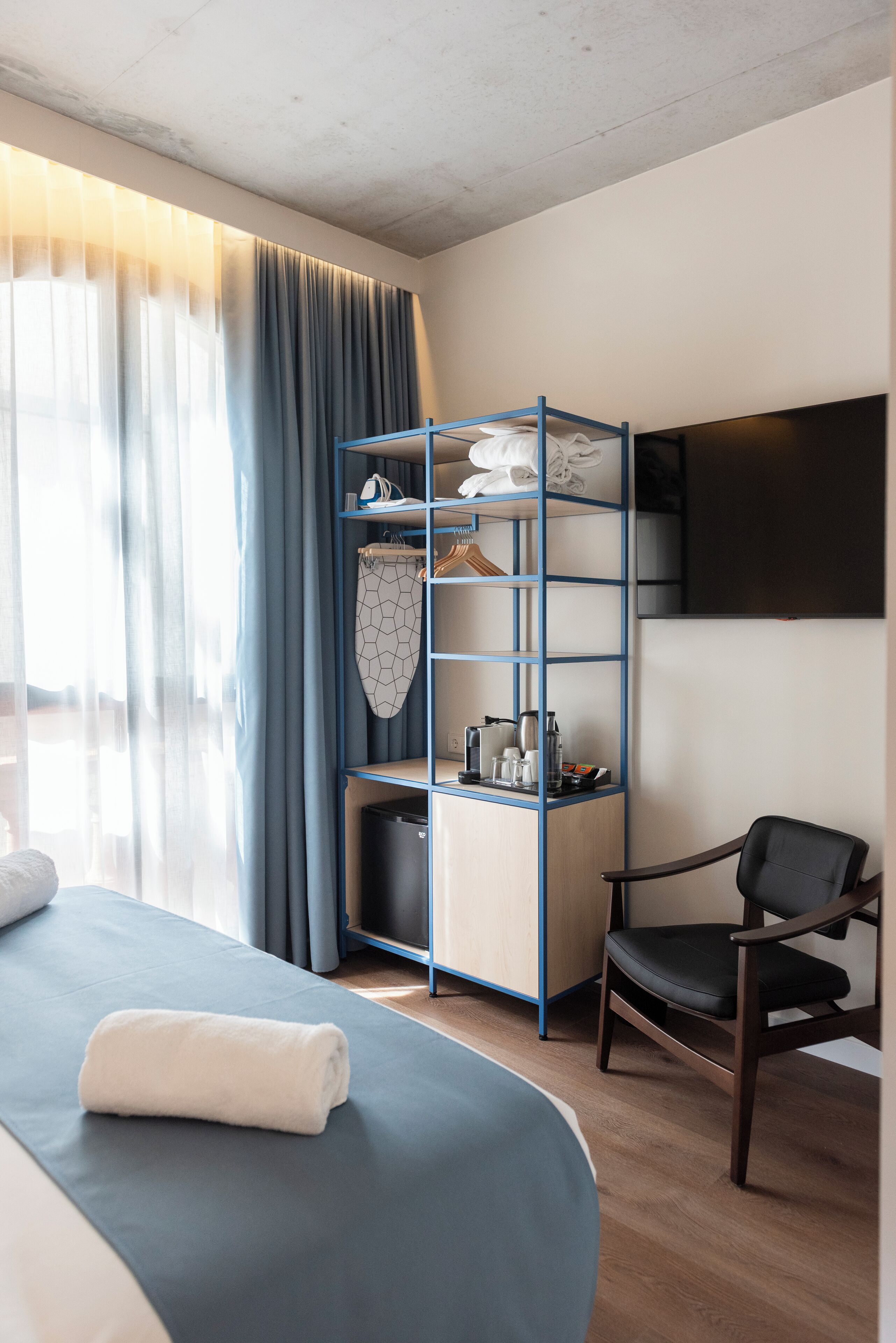 A hotel room with a bed, a chair, a wardrobe, and a flat-screen TV.