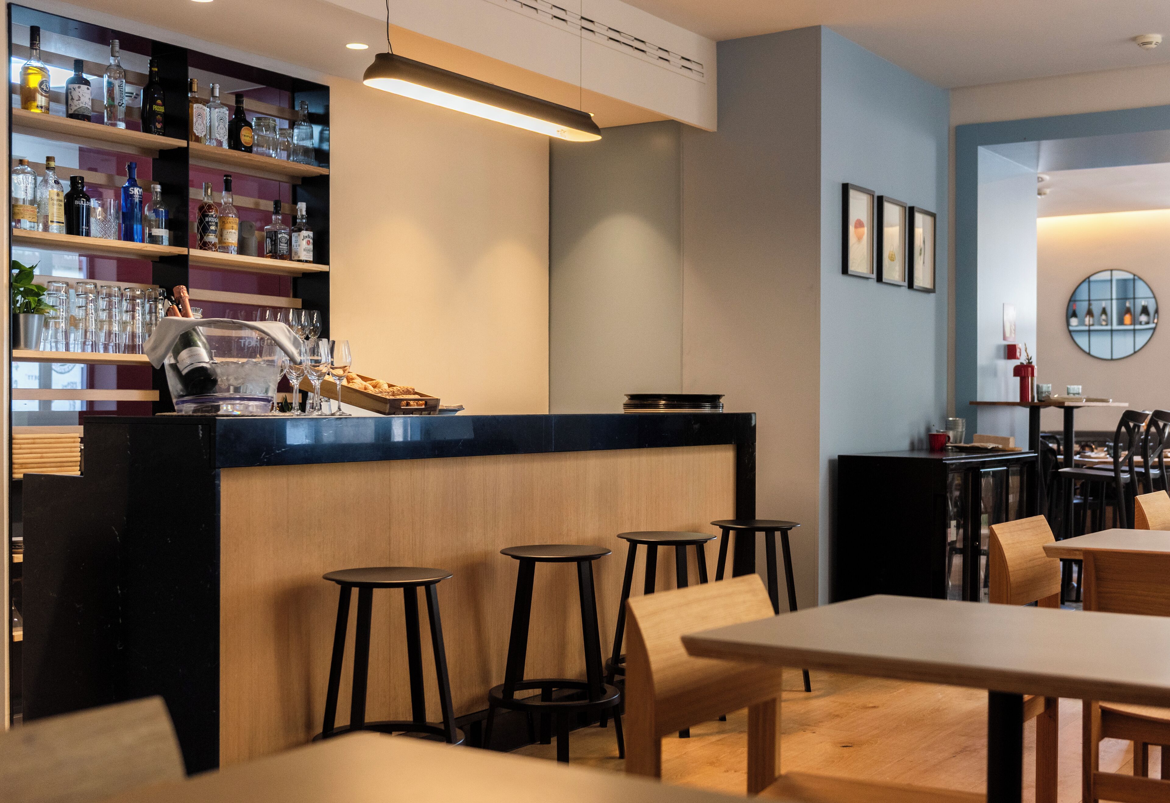 Una zona de bar con taburetes, una barra con botellas y cuadros en la pared.