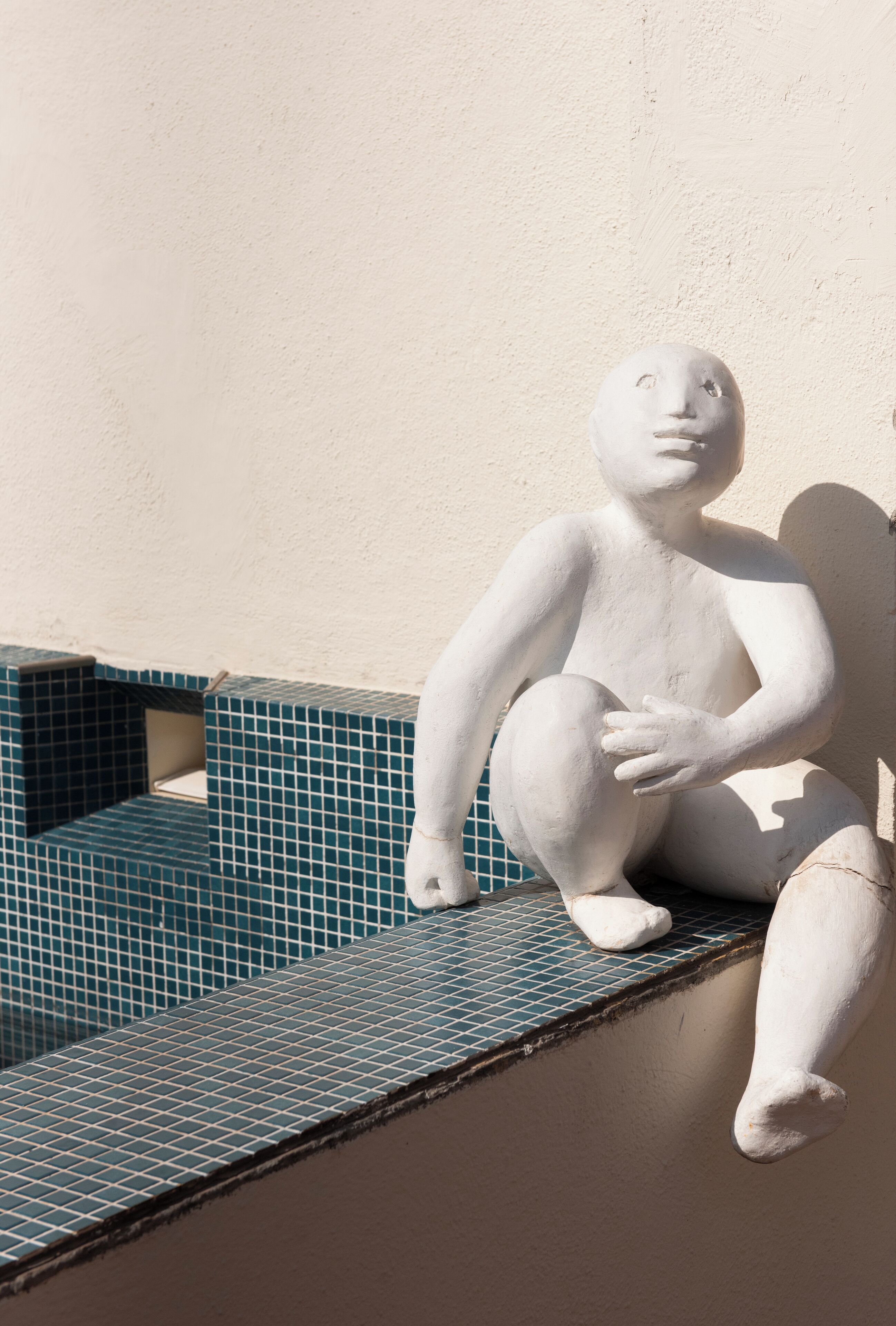 A white sculpture of a seated figure on a tiled ledge against a wall.
