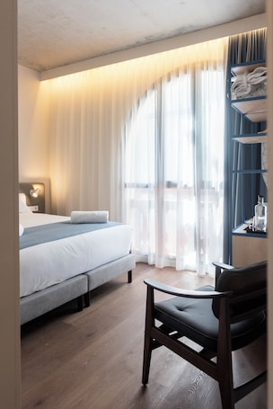 A hotel room with a bed, a chair, a nightstand, and a window with curtains.