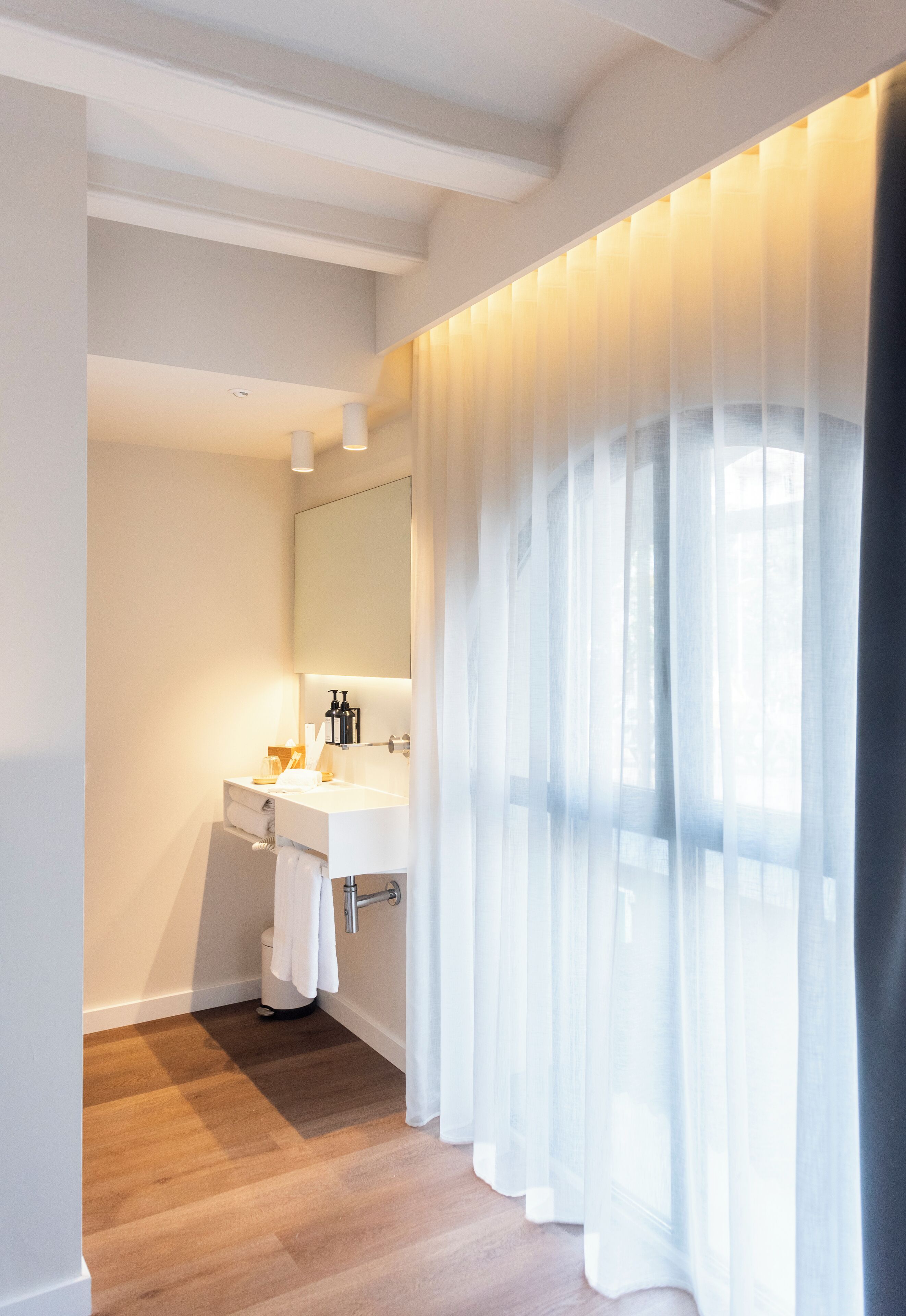 Un baño moderno con suelo de madera, un lavabo blanco y un espejo grande.