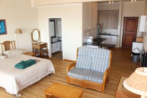 Una habitación con cama, sofá, una mesita, espejo y una pequeña cocina.