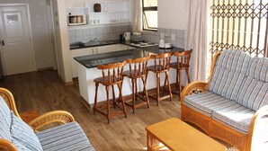 Een kleine keuken met een centraal eiland, houten stoelen, een bank en een eettafel.