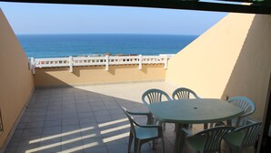 Een balkon met uitzicht op zee, een ronde tafel met stoelen en een witte balustrade.