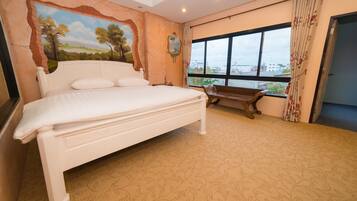 A bedroom with a large bed, a bench, a view of the city, and a mural on the wall.