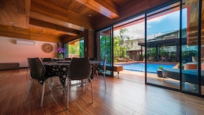 A modern dining area with a wooden ceiling, large windows, and a view of an outdoor swimming pool. - Thongtara House Boutique Residence (Samut Prakan)