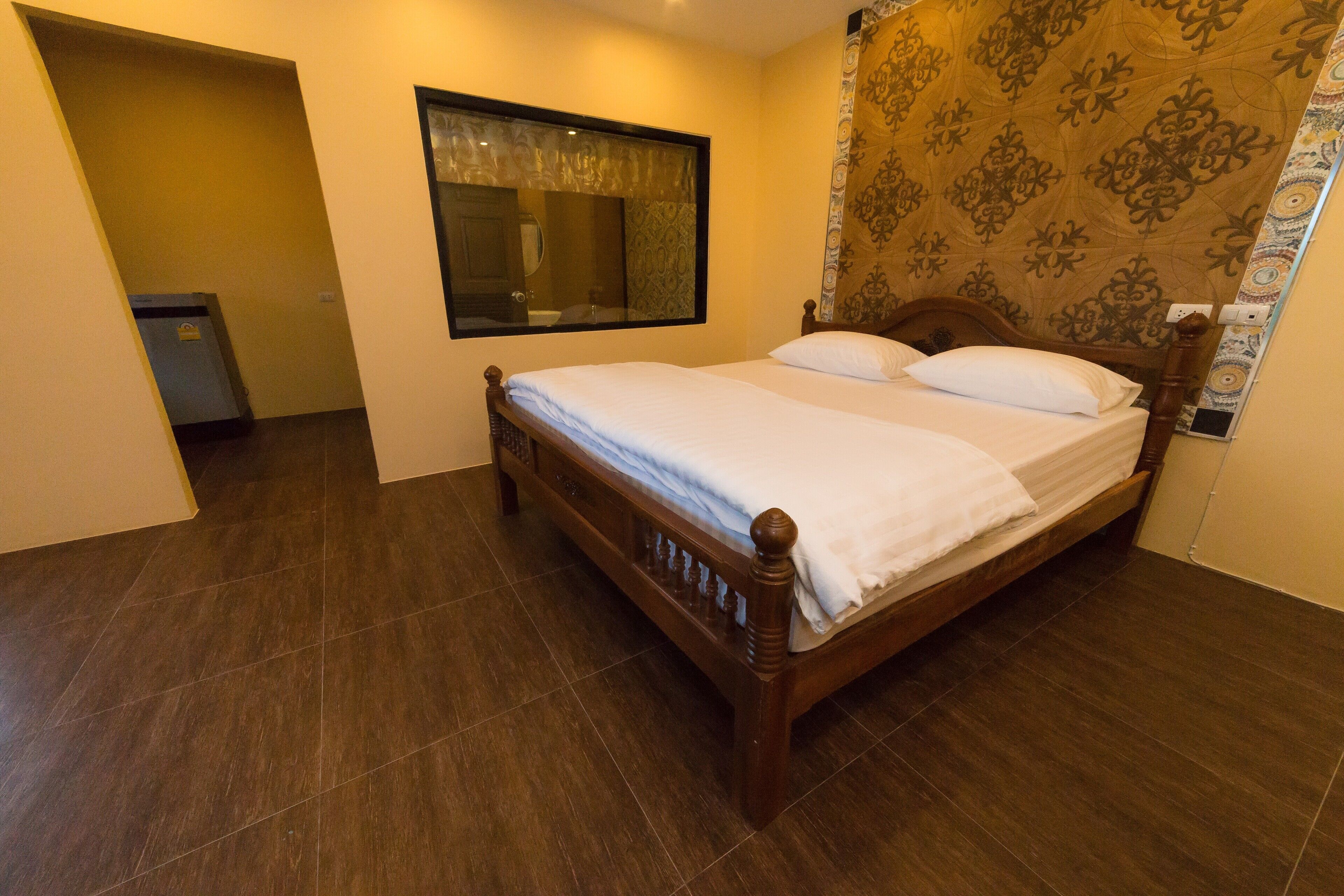 Un letto rifatto con cura in una camera d'albergo, con uno specchio grande sopra, pavimento in legno scuro e carta da parati decorata.