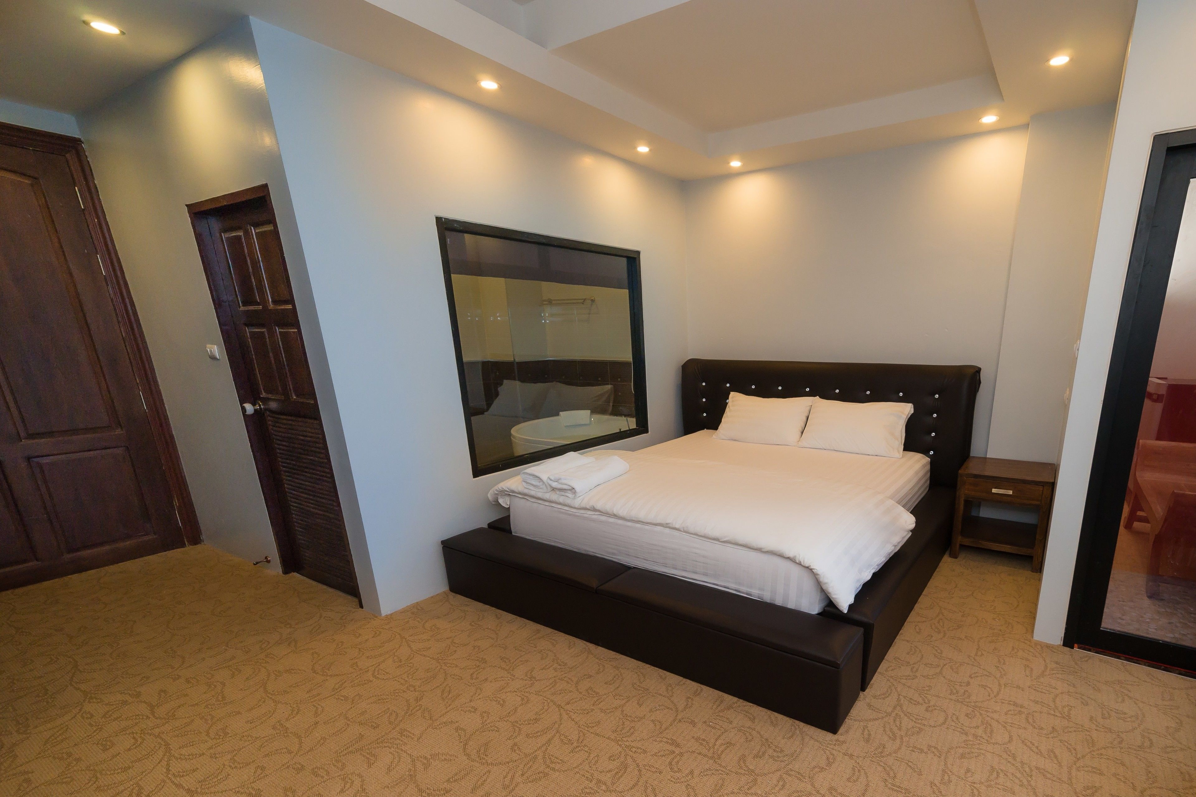 A neatly arranged bedroom with a bed, a bedside table, a mirror, and a door.