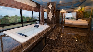 A modern bathroom with a large bathtub, a shower area, and a bed with a view of the city. - Thongtara House Boutique Residence (Samut Prakan)