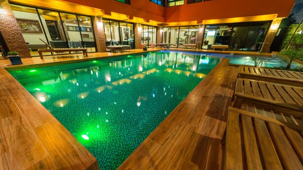 An indoor swimming pool with wooden deck areas and lounge chairs. - Thongtara House Boutique Residence (Samut Prakan)