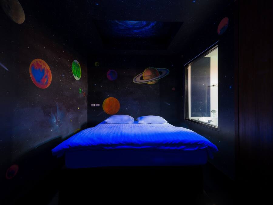 A bedroom with a bed, a window, and a wall decorated with planets.