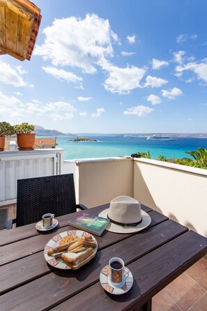 Una mesa de madera con un plato de pan, una taza de café y un sombrero en un balcón con vista a un mar turquesa y islas distantes.