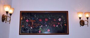 Una obra de arte enmarco con diseños florales y texto, sobre una pared, flanqueada por lámparas de pared.
