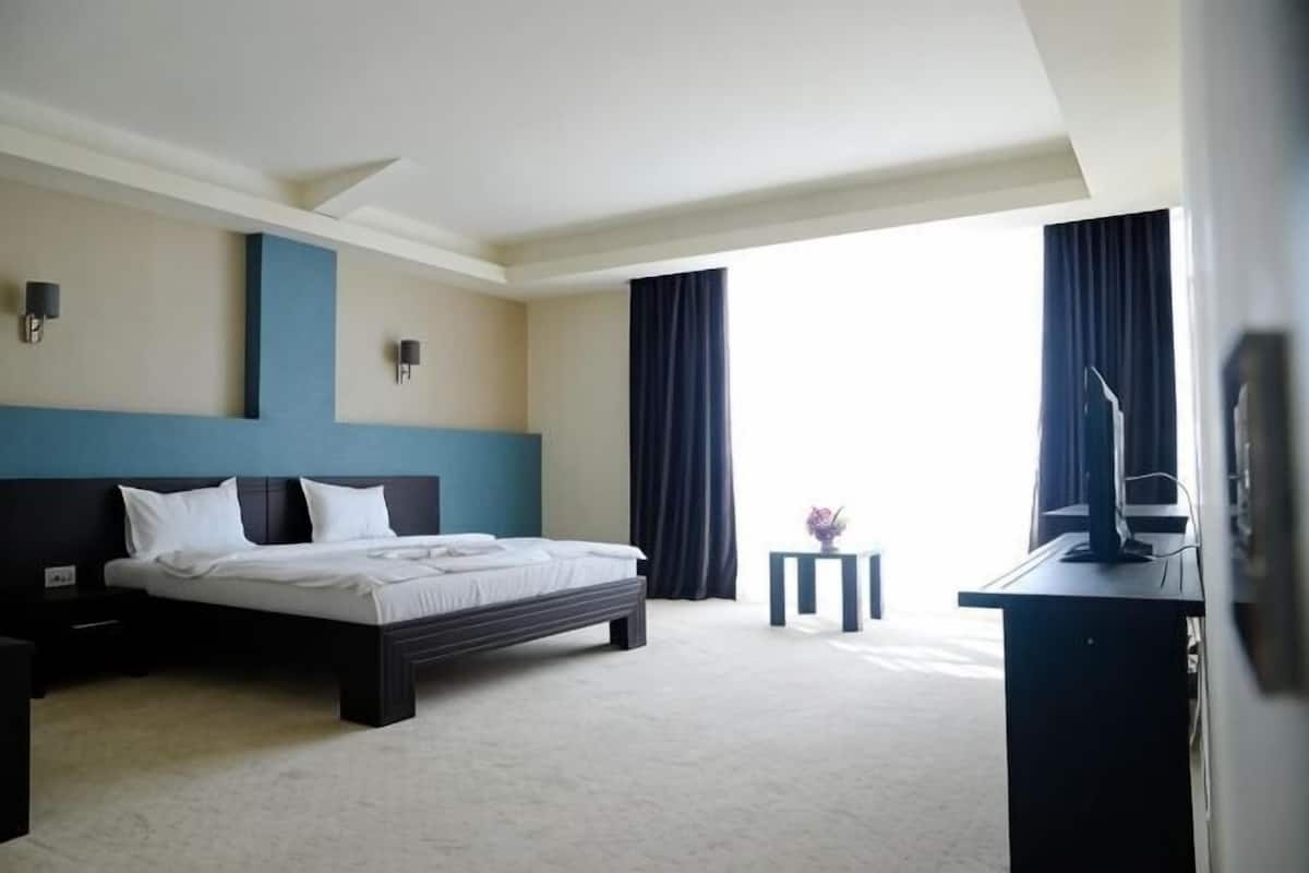 A hotel room with a bed, bedside tables, a desk, and a view of the outdoors.