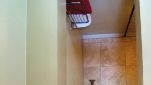 Un escalier recouvert de carreaux beiges, avec une rambarde métallique sur le côté gauche, une petite table avec une bougie sur le côté droit, et un tissu rouge suspendu au-dessus de la rambarde.