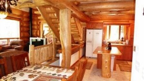 A cabin interior with a wooden dining table, a sofa, a refrigerator, and a kitchen area. - Elk Creek Lodge 3 Bedroom Holiday Home By Pinon Vacation Rentals (Salida)