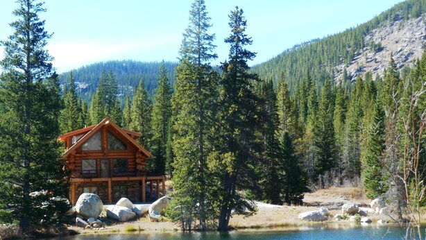 A log cabin with a deck, surrounded by a forest and a lake. - Elk Creek Lodge 3 Bedroom Holiday Home By Pinon Vacation Rentals (Salida)