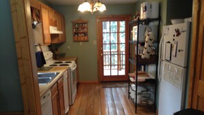 A kitchen with wooden cabinets, a stove, a refrigerator, and a window with a view of greenery. - Forest Creek Cabin 3 Bedroom Holiday Home By Pinon Vacation Rentals (Monarch)