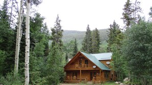 A log cabin with a porch, surrounded by dense forest and mountains. - Forest Creek Cabin 3 Bedroom Holiday Home By Pinon Vacation Rentals (Monarch)