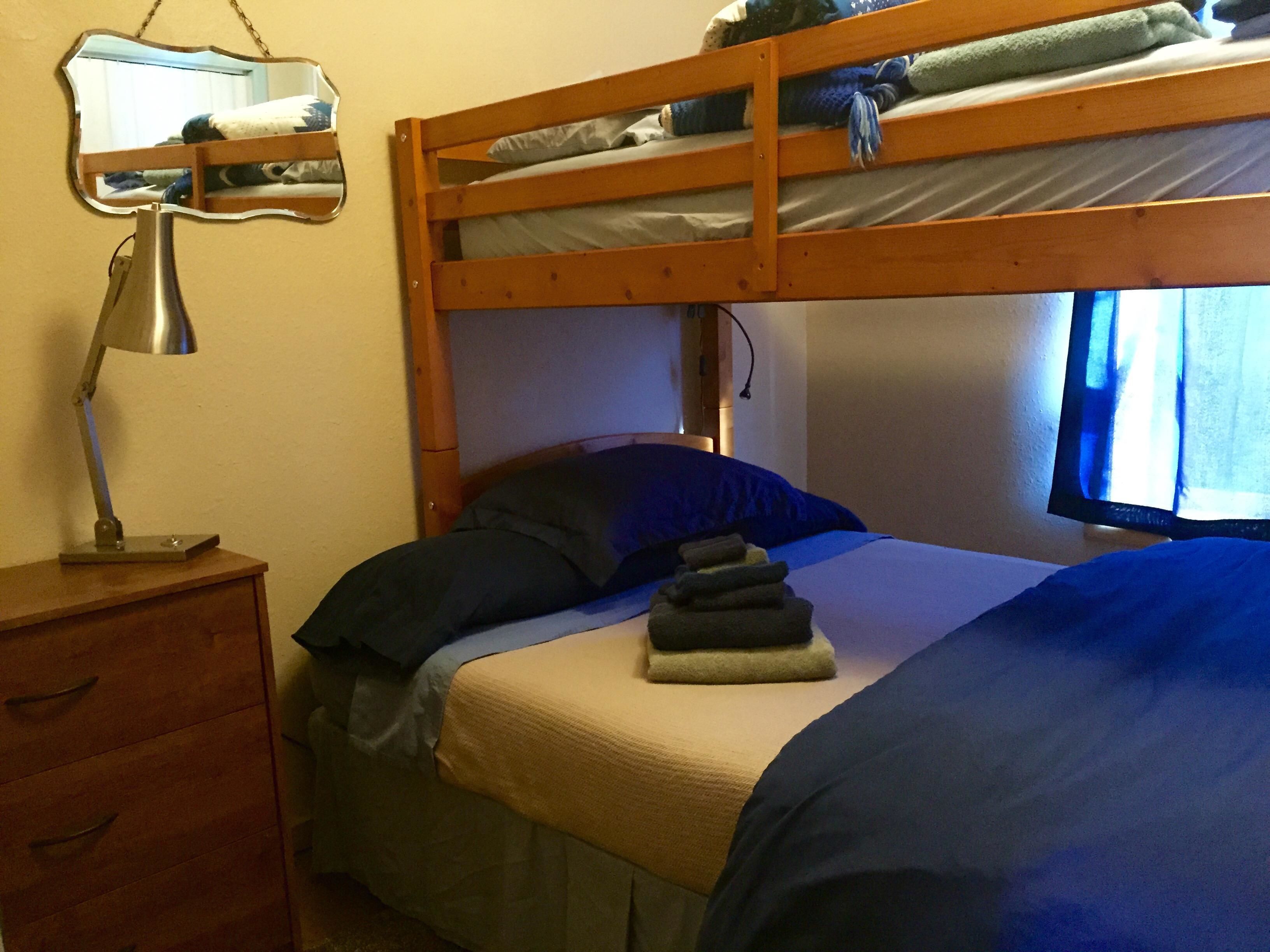 Ein Stockbett mit Schreibtisch und Stuhl, einer Lampe und einem Fenster mit Vorhängen.