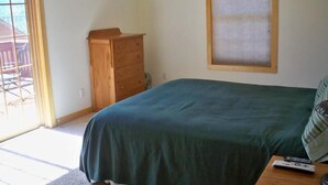 Een slaapkamer met een bed, een houten dressoir, een raam met zonwering en een tafeltje met een afstandsbediening.