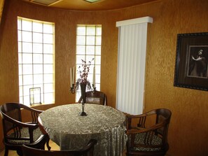 A dining area with a round table, four chairs, a vase with flowers, and a framed picture on the wall.