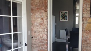 Une pièce avec un mur en briques, une porte blanche, un lavabo blanc et un tableau accroché au mur.
