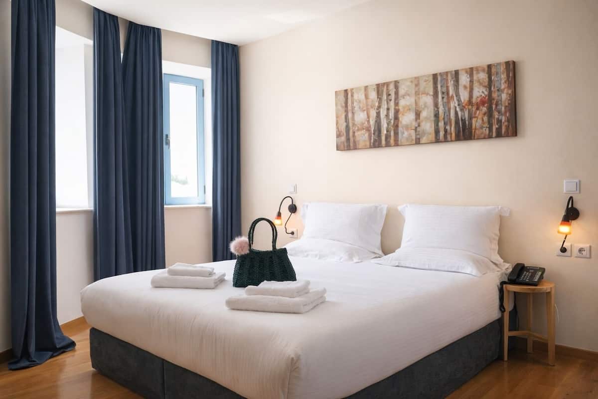 A neatly made bed with white linens, a green bag, and a painting on the wall.