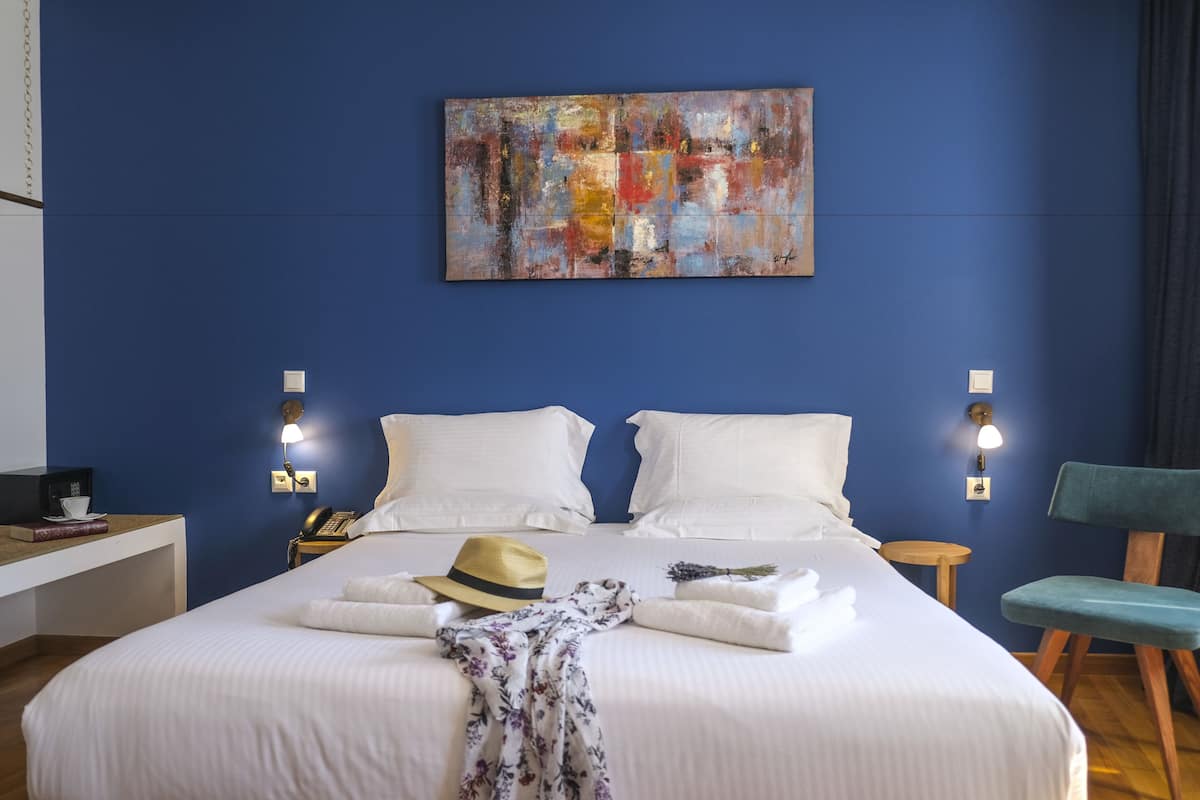 A hotel room with a large bed, two bedside tables, a desk, a chair, and a wall-mounted abstract painting.