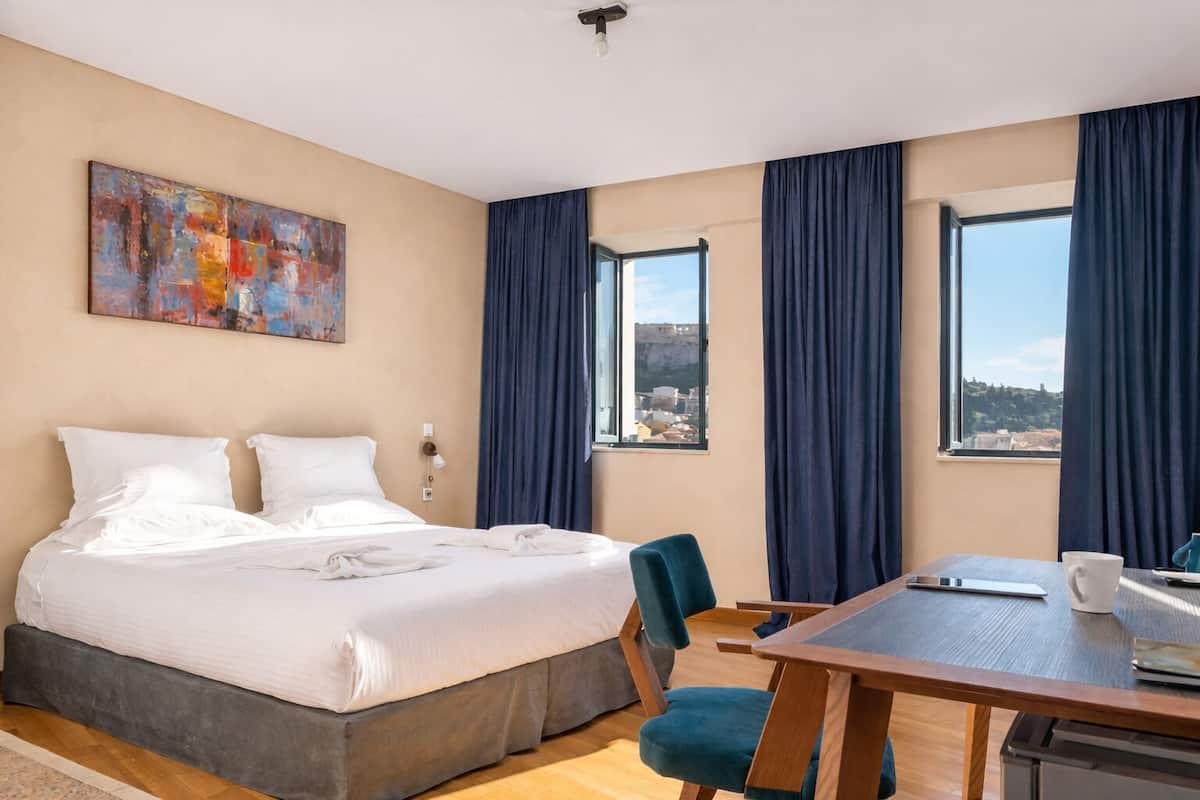 A hotel room with a bed, a desk, and a view of a cityscape.
