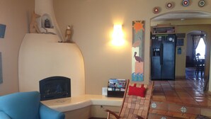Un salon avec un fauteuil bleu, un fauteuil à bascule en bois, une cheminée et un réfrigérateur à l’arrière-plan.