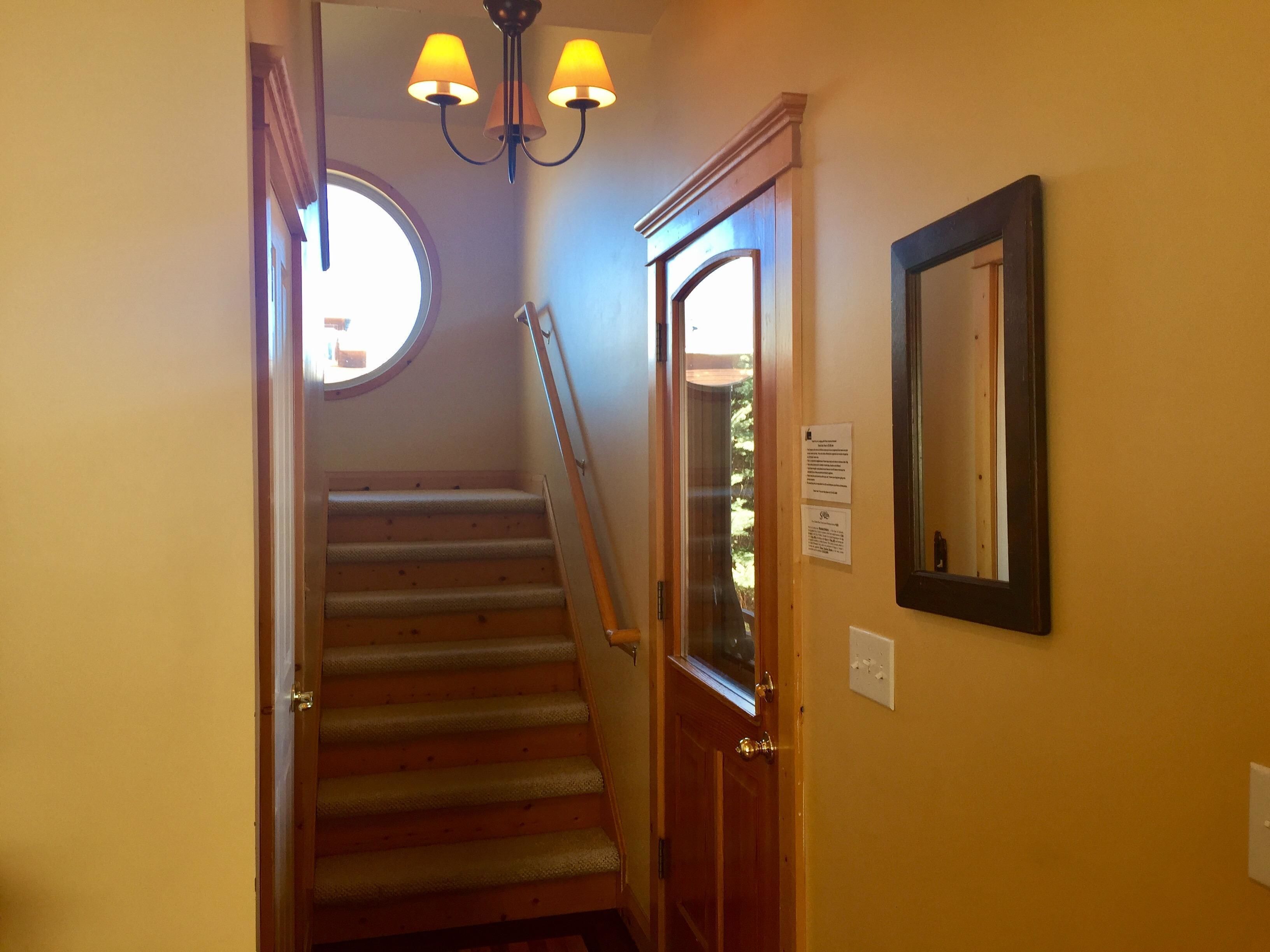 A staircase with a wooden handrail, a round window at the top, and a door with a glass panel.