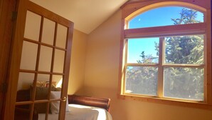 Une chambre avec une grande fenêtre, un lit et une porte en bois.