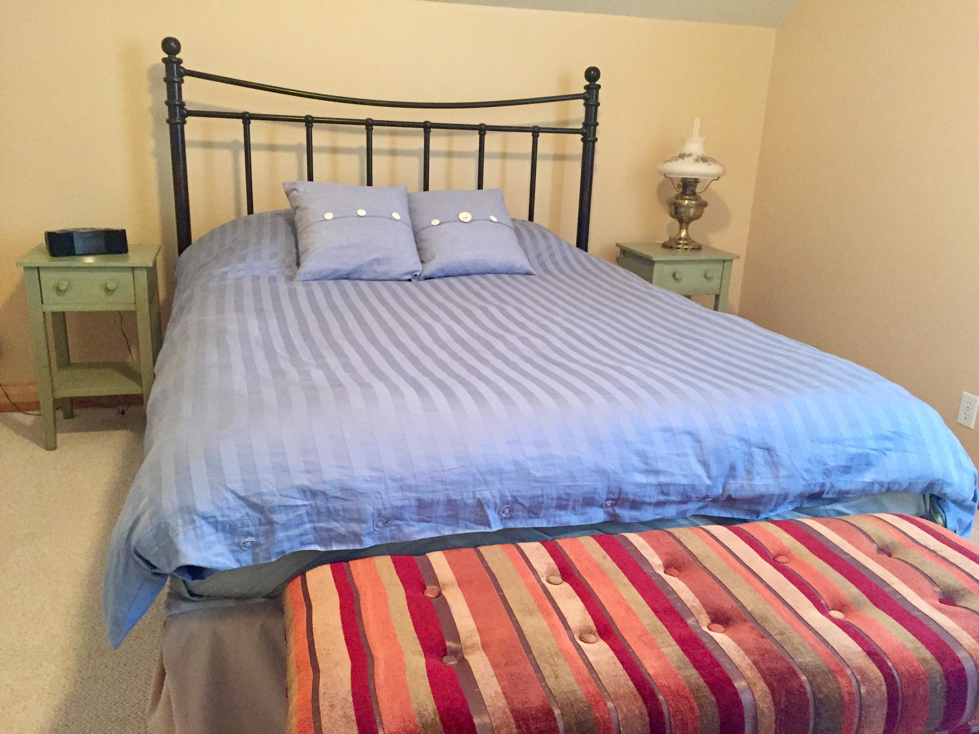 A bed with a metal frame, two pillows, a striped blanket, a bedside table, and a lamp.