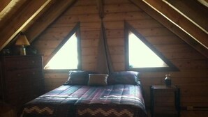 A cozy attic bedroom with a wooden ceiling, a bed with a patterned bedspread, two windows, and a dresser. - Mt Princeton Escape 1 Bedroom Holiday Home By Pinon Vacation Rentals (Nathrop)