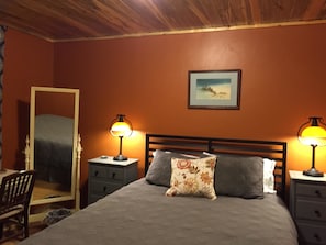 A bedroom with a bed, two bedside tables with lamps, a dresser, a chair, and a painting on the wall.