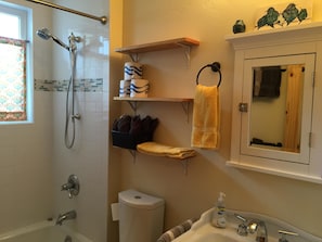 A bathroom with a shower, toilet, sink, and towel racks.
