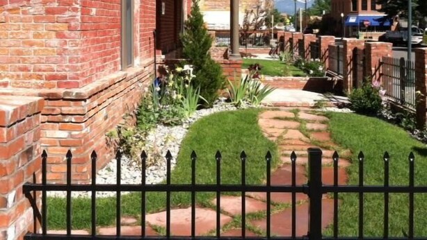 A brick building with a covered porch, a paved pathway, and a fenced garden area.