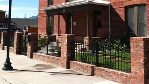 A red brick building with a covered porch and a black metal fence.