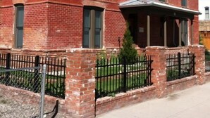 A red brick building with a flat roof, multiple windows, and a small porch area.
