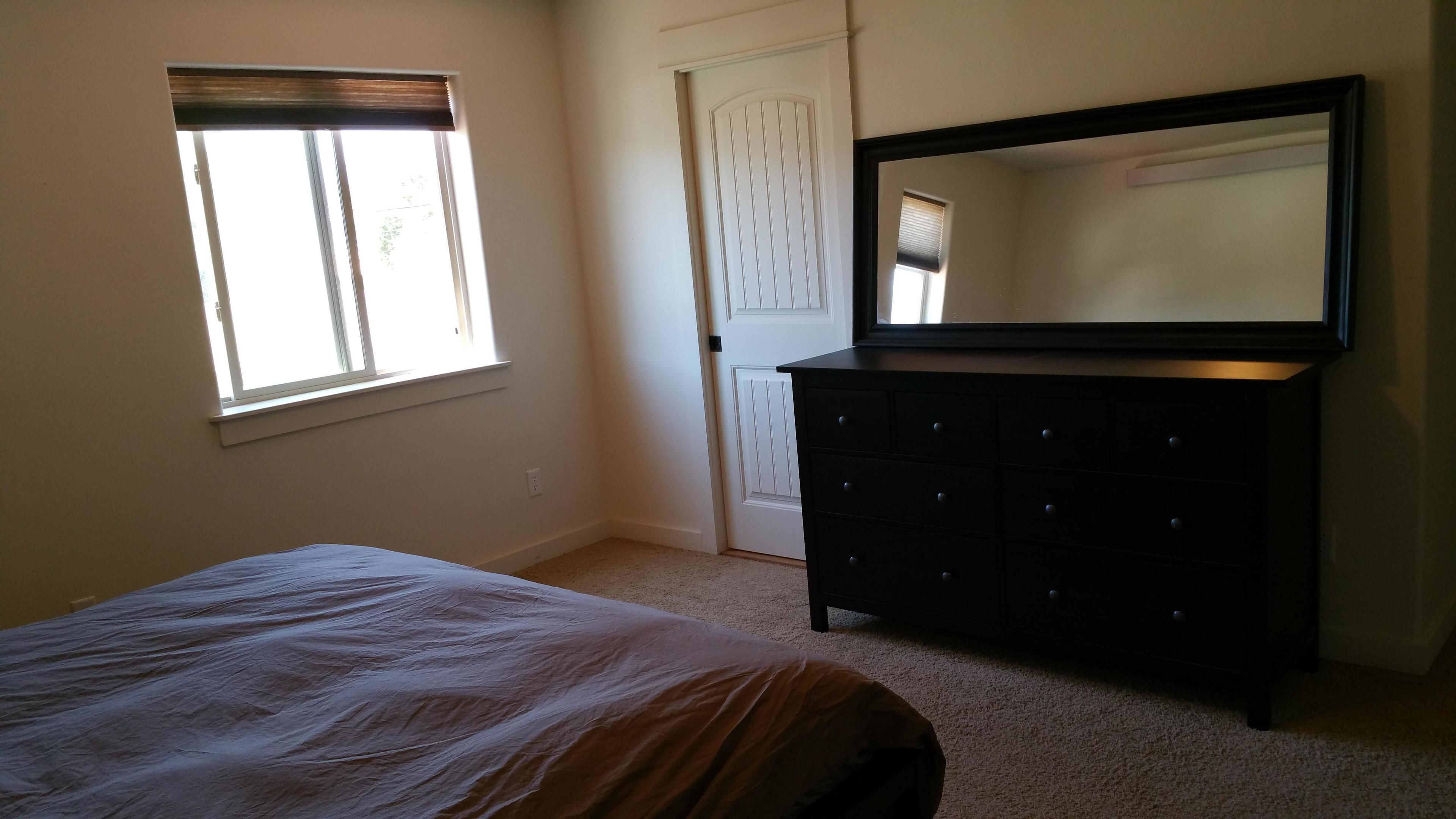 Une chambre à coucher avec un lit, une commode, une fenêtre et une porte.