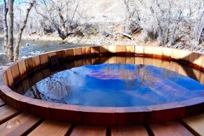 Una bañera de hidromasaje de madera con borde curvo, rodeada por una terraza de madera.