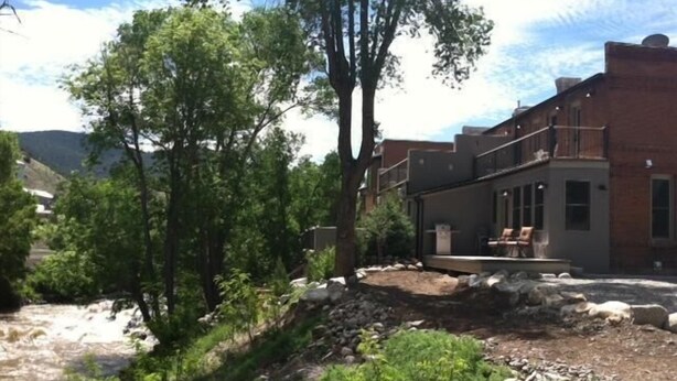 A two-story building with a brick facade, a balcony, and a stone retaining wall. - River House Upstream 2 Bedroom Holiday Home By Pinon Vacation Rentals (Salida)