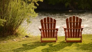 Two wooden Adirondack chairs facing a body of water with a grassy area and some bushes in the foreground. - River House Upstream 2 Bedroom Holiday Home By Pinon Vacation Rentals (Salida)