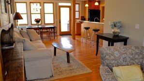 A living room with a sofa, a coffee table, and a patterned armchair. There is a dining area with a table and chairs, and a kitchen area with a counter and stools. - River House Upstream 2 Bedroom Holiday Home By Pinon Vacation Rentals (Salida)