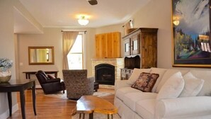 A living room with a fireplace, a white sofa, a wooden cabinet, and a painting on the wall. - River House Upstream 2 Bedroom Holiday Home By Pinon Vacation Rentals (Salida)