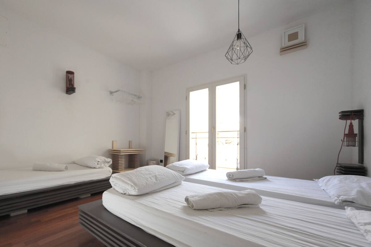 A hotel room with two beds, a large window, and a hanging light fixture.