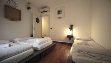 Een kamer met drie eenpersoonsbedden, houten vloeren, een wandairconditioner, een ingelijst schilderij en een wandlamp.
