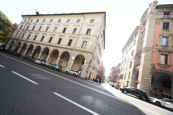 A street with parked cars and historic buildings with arched windows and balconies.