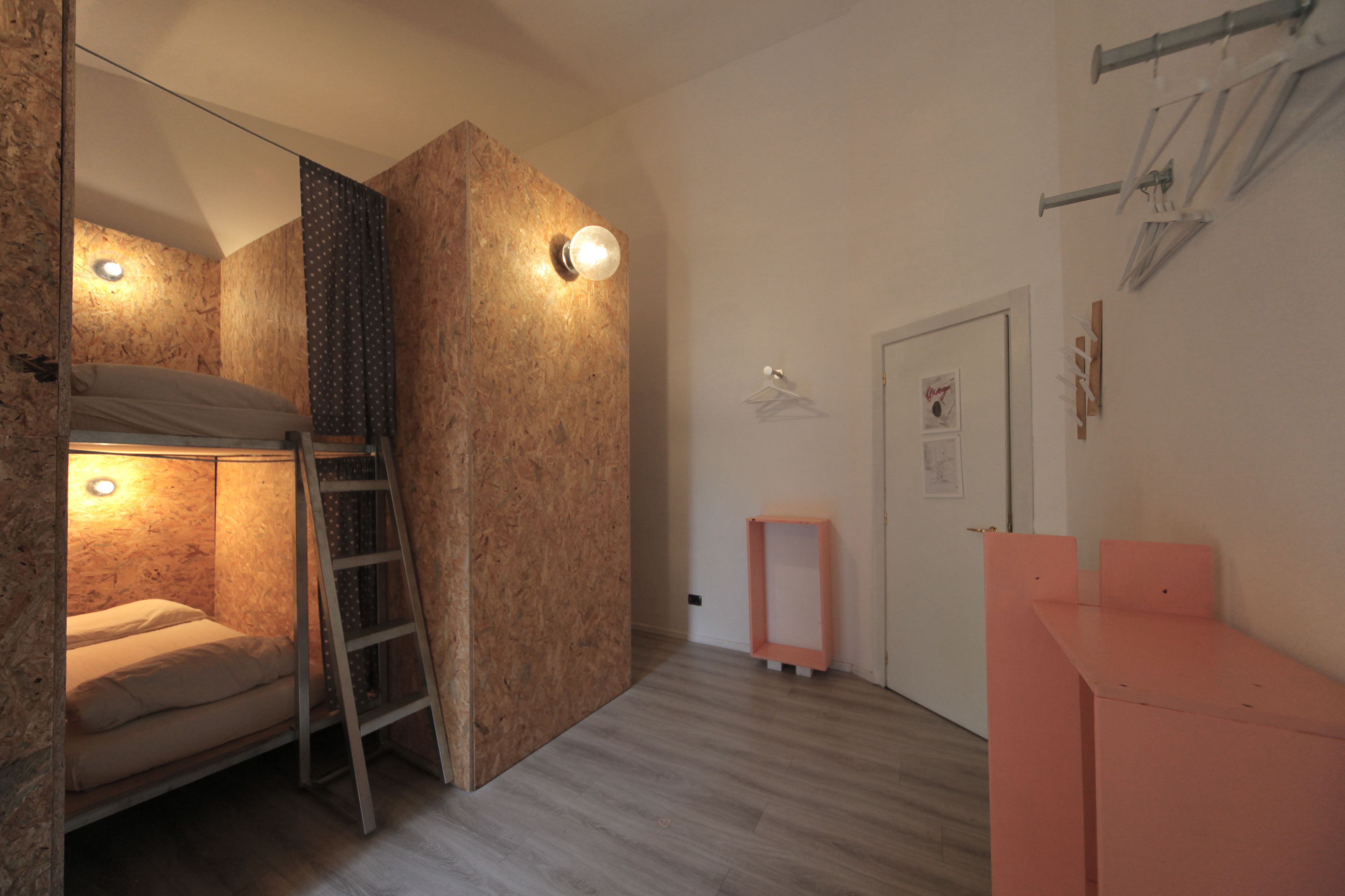 Una habitación con una cama litera, una escalera, una pequeña mesa rosa y una puerta con un perchero en la pared.